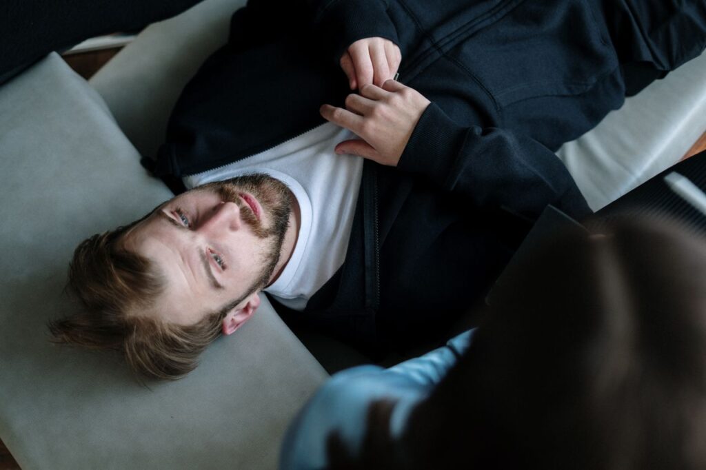 pexels-photo-4101177 A bearded man lying down during a therapy session indoors, expressing emotions.